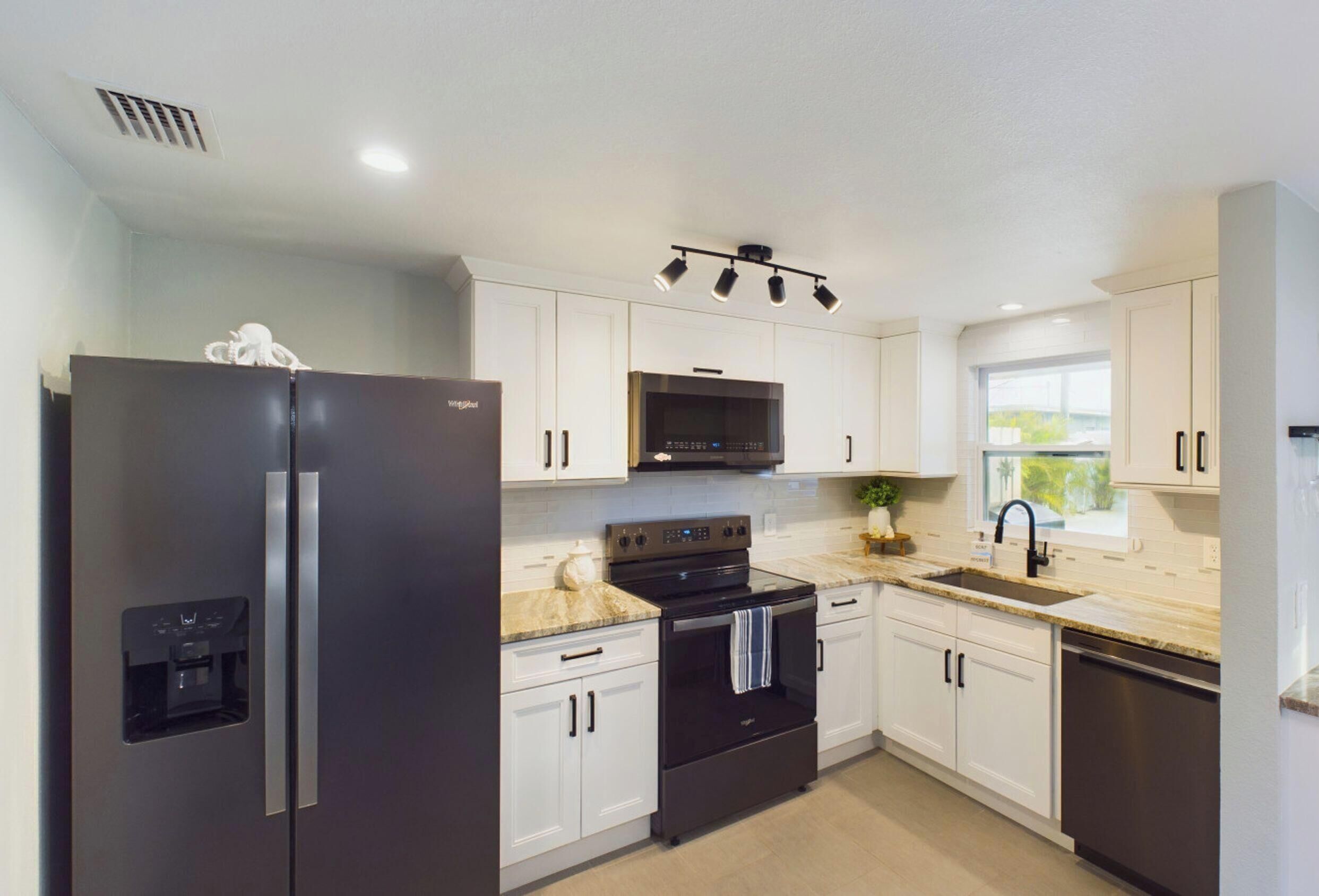 A modern kitchen with white cabinets, a black refrigerator, a stove, and a sink.