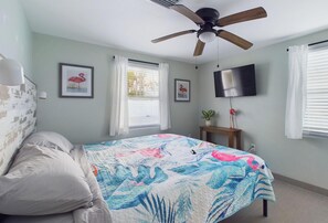 A bedroom with a bed, a ceiling fan, a TV, and a window with curtains. - Castaway Cottage Beautiful Pool Spa Steps 2 Sand Restaurants Golf Cart Included (Holmes Beach)