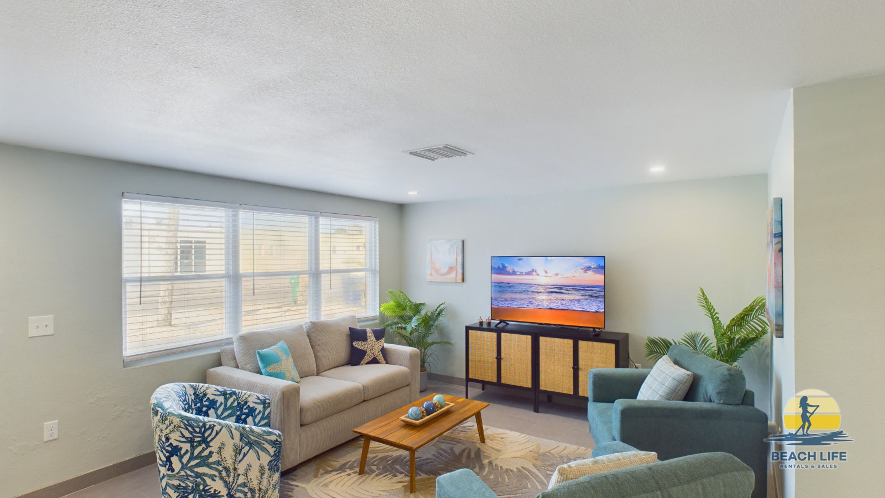 A living room with a sofa, armchairs, a coffee table, a TV, and a window with blinds.