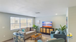 A living room with a sofa, armchairs, a coffee table, a TV, and a window with blinds. - Castaway Cottage Beautiful Pool Spa Steps to Sand Restaurants Golf Cart Included (Holmes Beach)