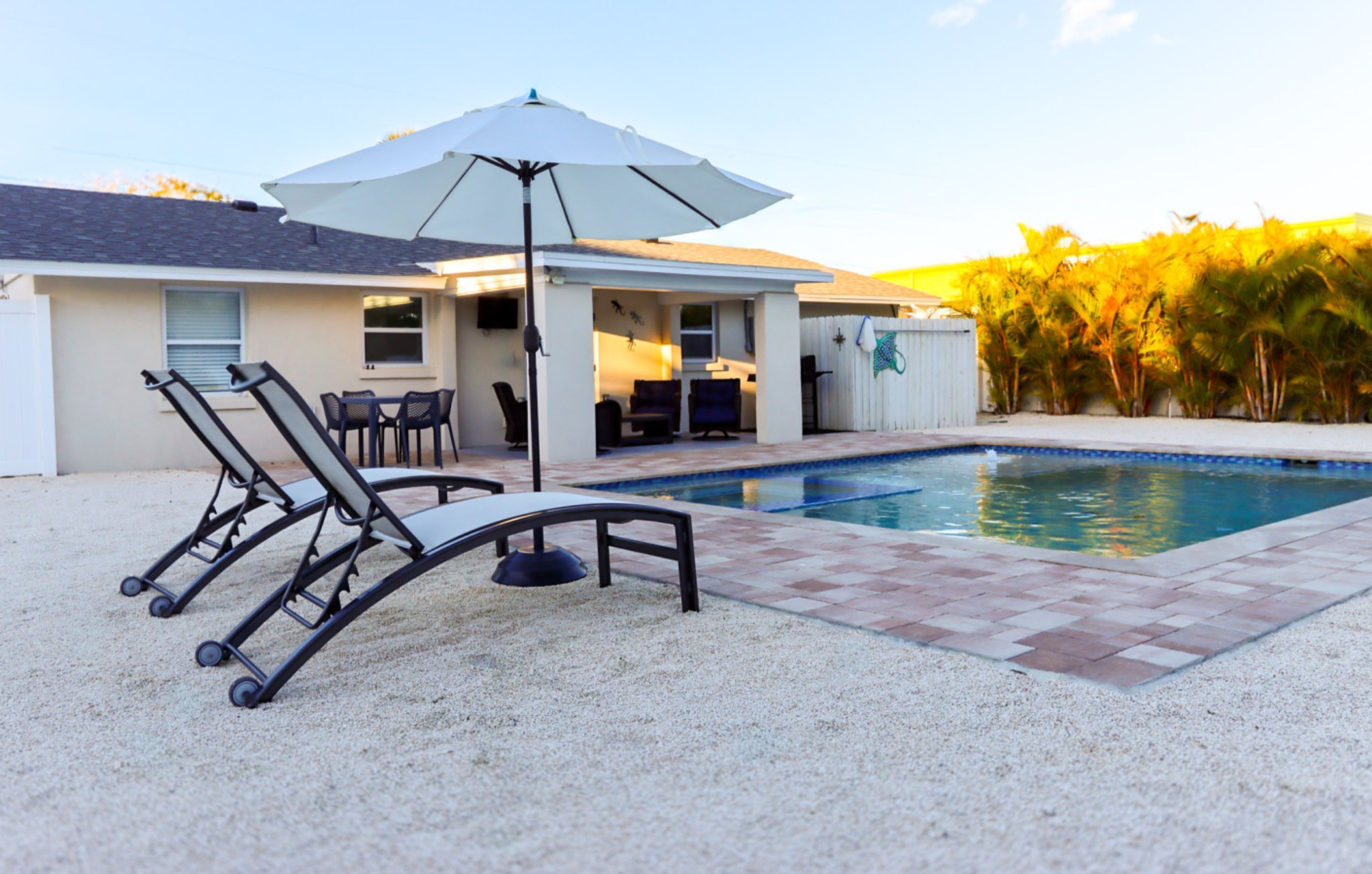 A backyard with a swimming pool, patio furniture, and a covered seating area.
