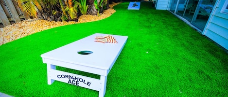 Un jeu de «
cornhole
» installé sur une pelouse artificielle, avec une table blanche et un drapeau rouge.