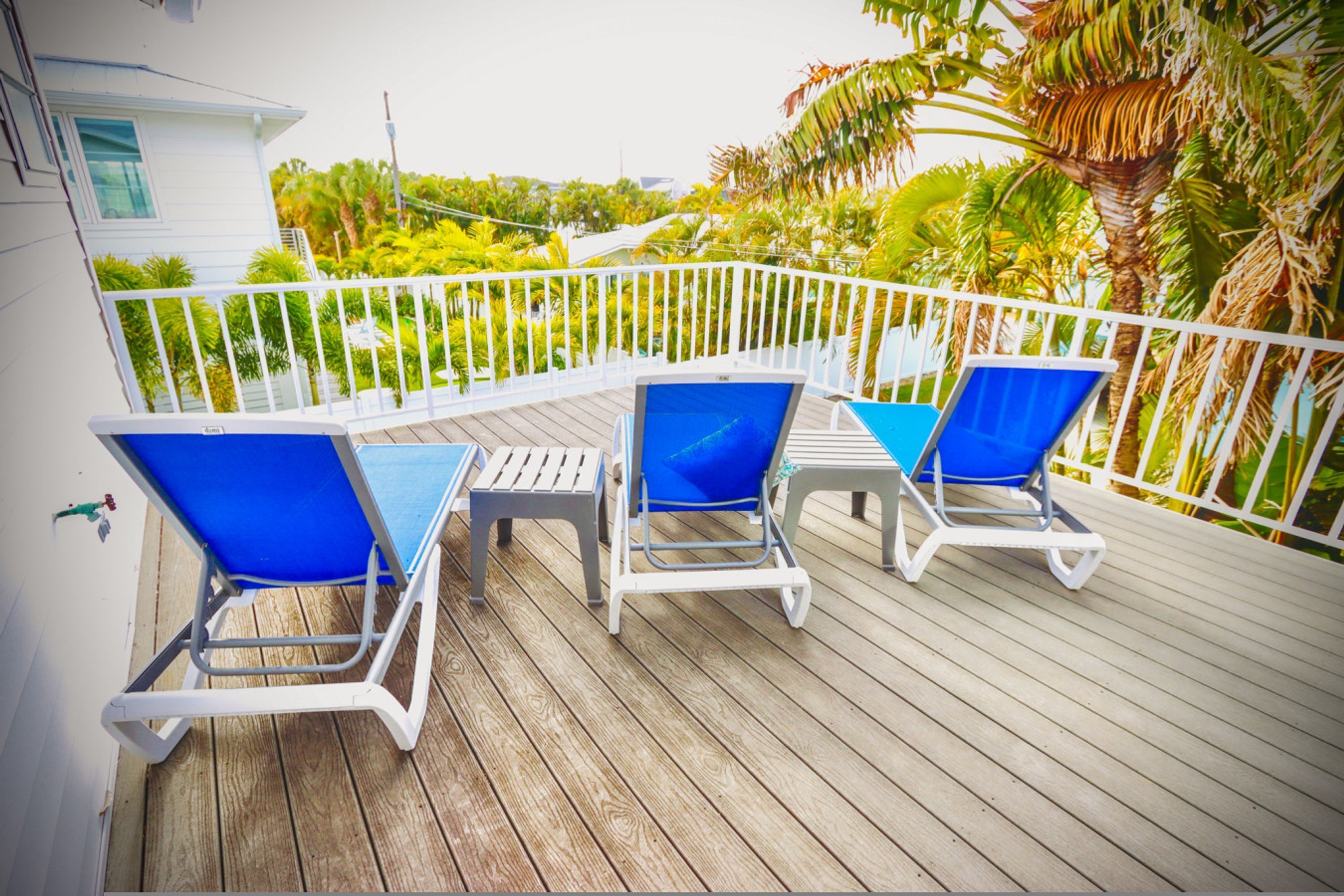 A wooden deck with a white railing, three blue lounge chairs, and a small table.