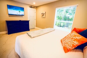 Ein Schlafzimmer mit einem Bett, einem Schminktisch, einem an der Wand befestigten Fernseher und einem Fenster mit Jalousien.