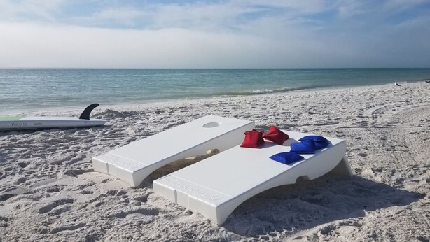 Una spiaggia con due lettini bianchi, uno con cuscini rossi e blu, e una tavola da surf.
