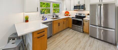 A modern kitchen with stainless steel appliances, wooden cabinets, and a window with a view of greenery.