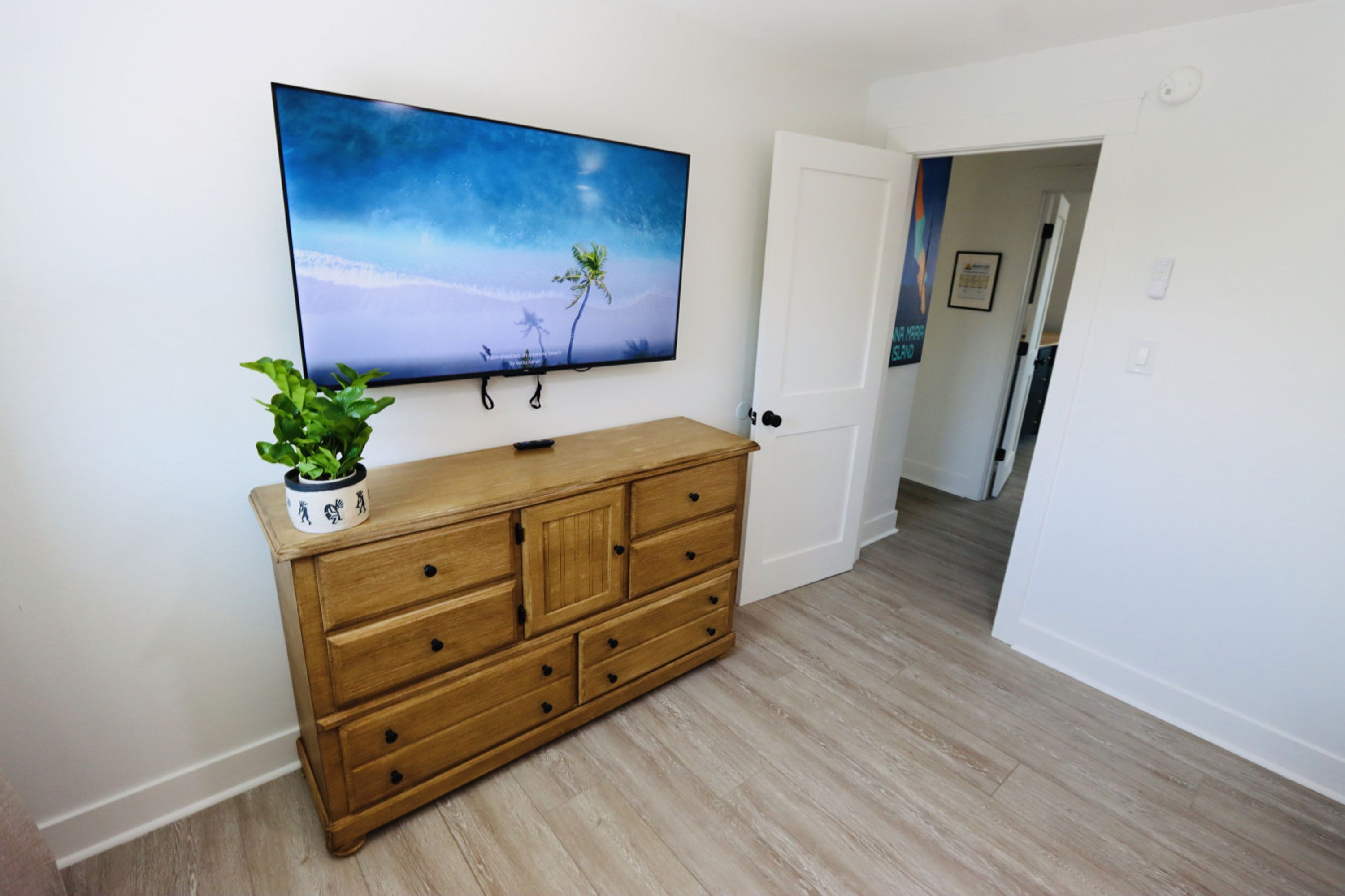 A room with a wooden dresser, a flat-screen TV mounted on the wall, and a potted plant on the dresser.
