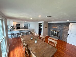 Un comedor amplio con una mesa y sillas de madera, una cocina al fondo y una chimenea de piedra con un cartel encima.