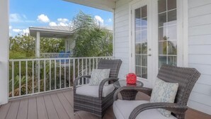 A covered porch with wicker furniture and a glass door. - Fairwinds Tropical Getaway With Pool Hot Tub Game Room Steps to Gulf Beaches (Holmes Beach)