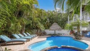 A swimming pool with lounge chairs and a thatched umbrella, surrounded by tropical vegetation. - Fairwinds Tropical Getaway With Pool Hot Tub Game Room Steps to Gulf Beaches (Holmes Beach)