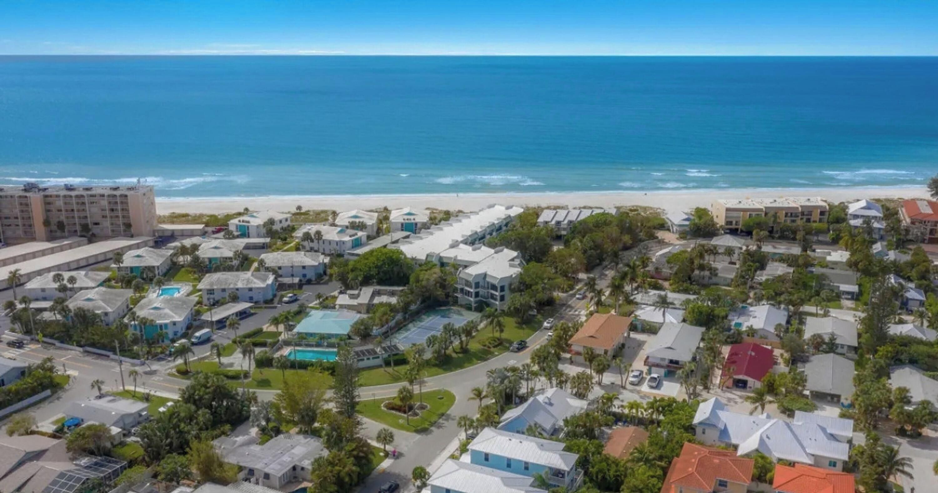 A coastal residential area with a beachfront, houses with varying roof colors, and a large hotel building.