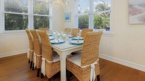 A dining room with a glass-top table, wicker chairs, and a chandelier. - Fairwinds Tropical Getaway With Pool Hot Tub Game Room Steps to Gulf Beaches (Holmes Beach)