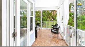 Ein überdachter Balkon mit Fliesenboden, weißen Geländern und zwei Korbstühlen.