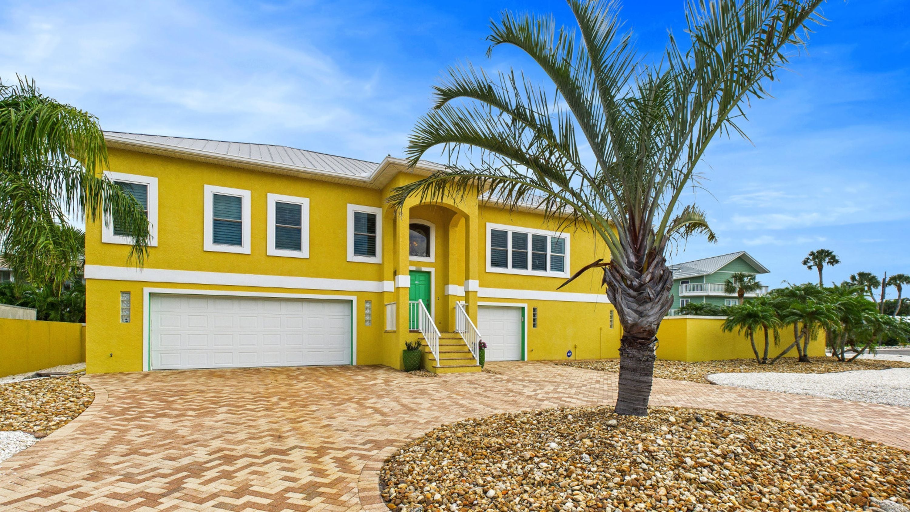 A yellow house with a garage, a staircase, and a palm tree in the front yard.