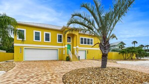 A yellow house with a garage, a staircase, and a palm tree in the front yard. - NEW Listing Barefoot Bliss Gulf Views Heated Pool Spa Golf Cart Incl Game Rm Tiki Bar Sleeps 8 (Holmes Beach)