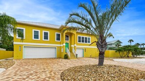 A yellow house with a garage, a staircase, and a palm tree in the front yard. - NEW Listing Barefoot Bliss Gulf Views Heated Pool Spa Golf Cart Incl Game Rm Tiki Bar Sleeps 8 (Holmes Beach)