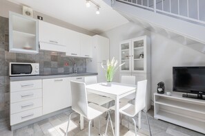 A modern kitchen with white cabinetry, a microwave, and a dining area with a white table and chairs. - Loft Lingotto by Wonderful Italy (Turin)
