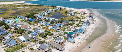 A coastal residential area with houses along the beach, a road, and a body of water.