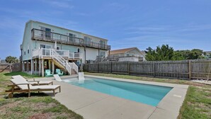 Ein zweistöckiges Haus mit Swimmingpool, überdachter Terrasse und Holzzaun.