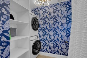 Un lavadero con papel tapiz floral azul, una lavadora Samsung y una secadora.