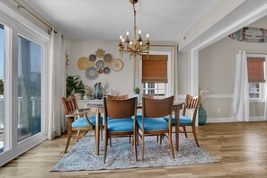 Ein Essbereich mit einer Chandelüster, Holzstühlen mit blauen Kissen, einem gemusterten Teppich und Wanddekoration.