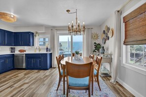 Una cocina moderna con gabinetes azules, un comedor con mesa y sillas de madera, y vistas a través de amplias ventanas.