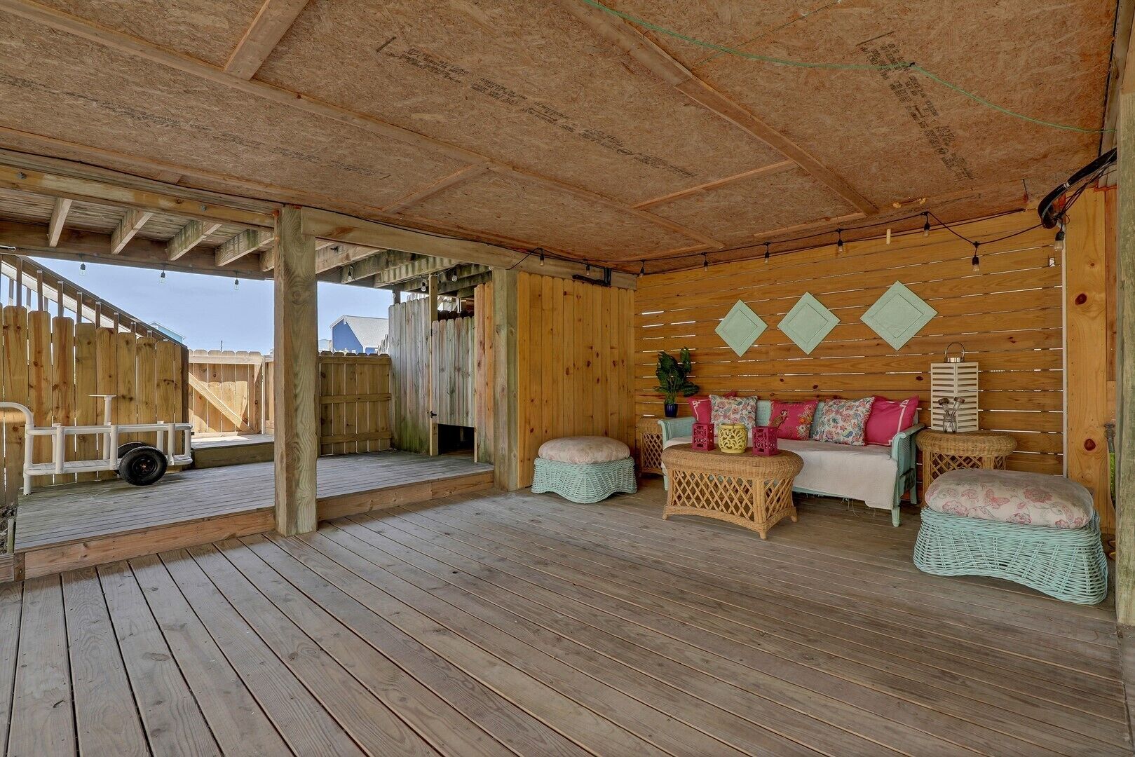 Un espacio de estar al aire libre techado, con piso de madera, un banco de madera, un sofá acolchado y una pequeña mesa.