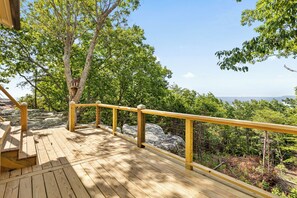 A wooden deck with a railing, overlooking a forested area with a clear sky.