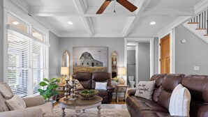 A spacious living room with a high ceiling, a ceiling fan, and a large painting of a barn. There are two leather sofas, a coffee table, and a side table with lamps. - McLemore Resort - 68 Founder Path - Walking distance to Range and Clubhouse (Rising Fawn)