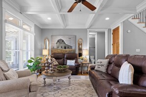 A spacious living room with a high ceiling, a ceiling fan, and a large painting of a barn. There are two leather sofas, a coffee table, and a side table with lamps. - McLemore Resort - 68 Founder Path - Walking distance to Range and Clubhouse (Rising Fawn)
