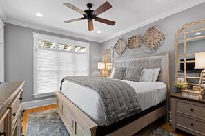 Ein Schlafzimmer mit einem Bett, einem Deckenventilator, einem Fenster mit Jalousien und einer Kommode.