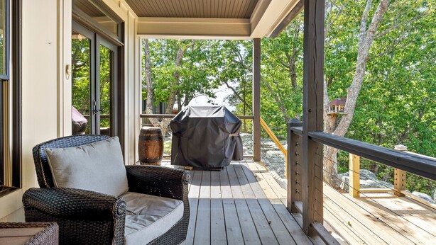 A covered outdoor area with a wooden deck, a grill, and a wicker chair. - McLemore Resort - 68 Founder Path - Walking distance to Range and Clubhouse (Rising Fawn)