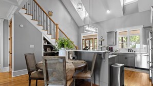 A modern kitchen with a central island, wooden flooring, and a staircase with a wooden railing. - McLemore Resort - 68 Founder Path - Walking distance to Range and Clubhouse (Rising Fawn)