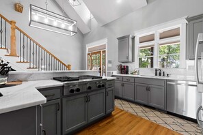 A modern kitchen with a central island, grey cabinetry, and a stainless steel range.