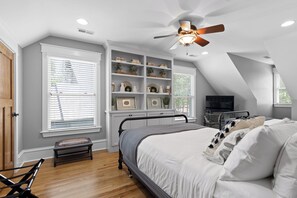 A bedroom with a sloped ceiling, a bed, a bench, a TV, and built-in shelving with decorative items.
