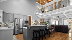A modern kitchen with stainless steel appliances, a central island with stools, and a dining area with a view. - McLemore Resort - 68 Founder Path - Walking distance to Range and Clubhouse (Rising Fawn)