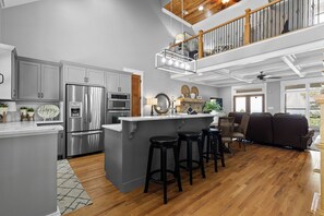 A modern kitchen with stainless steel appliances, a central island with stools, and a dining area with a view. - McLemore Resort - 68 Founder Path - Walking distance to Range and Clubhouse (Rising Fawn)