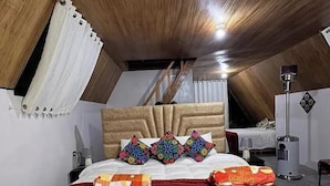 A bedroom with a sloped ceiling, a bed with colorful pillows, a striped blanket, and a bedside table with a lamp.