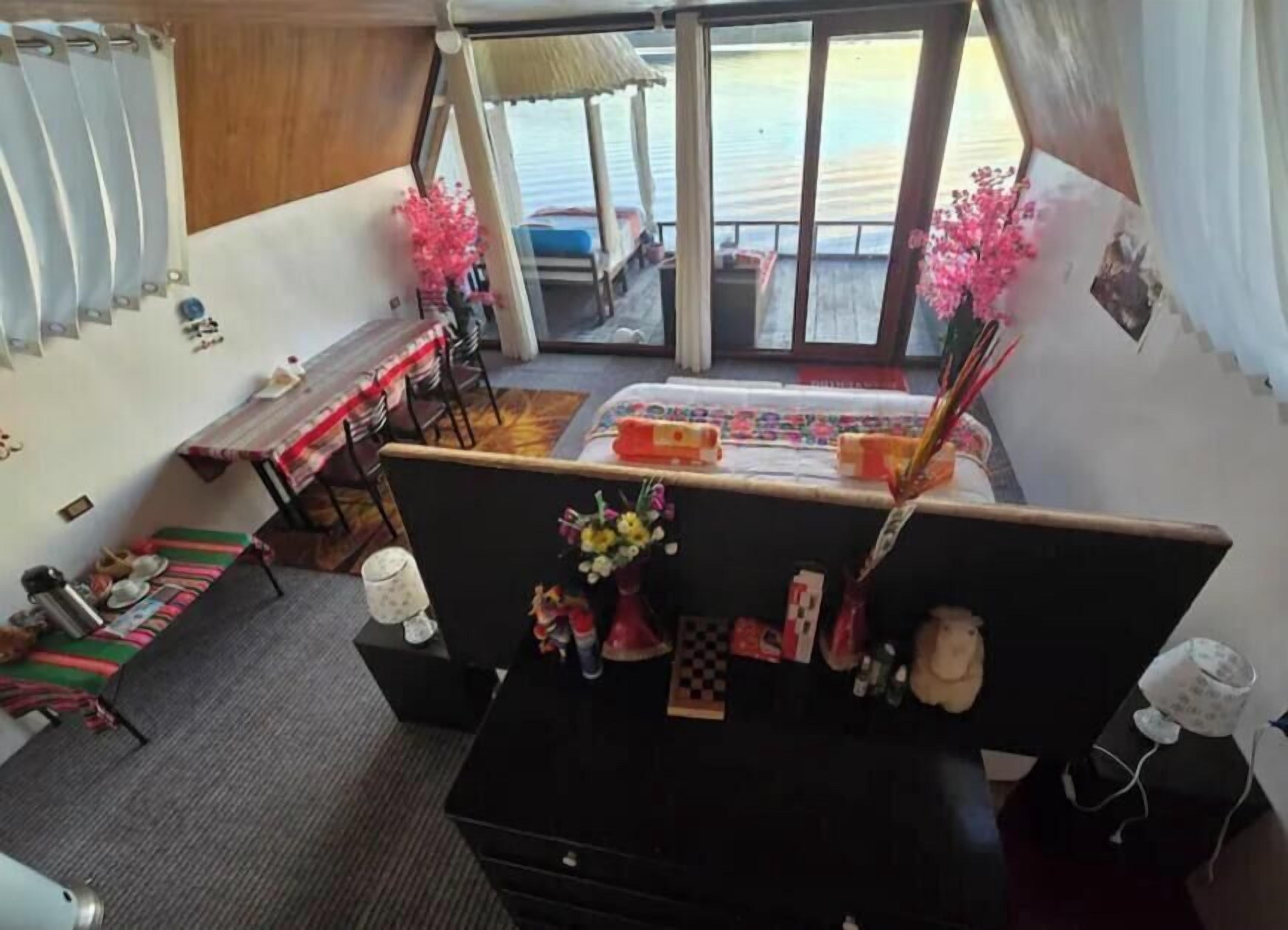 Une pièce comprenant un bureau, des chaises, une petite table, un lit et offrant une vue sur la mer grâce à de grandes fenêtres.