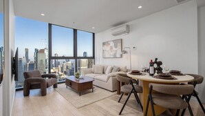 Uma sala de estar moderna com vista para a cidade, uma área de jantar com mesa e cadeiras redondas e um conjunto de sofás.