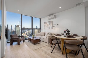 Ein modernes Wohnzimmer mit Blick auf die Stadt, eine Essecke mit rundem Tisch und Stühlen sowie eine Sofagarnitur.