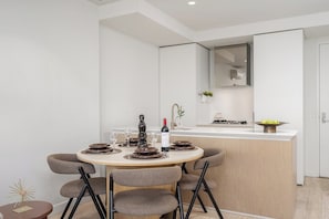 A modern dining area with a round table, chairs, and a kitchen counter in the background. - Sky-High 1BR, Panoramic City Views with Pool & Gym (Melbourne)