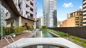 Um edifício moderno com piscina no terraço, cercado por edifícios altos.