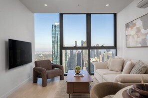 Ein modernes Wohnzimmer mit einem großen Fenster, einem Flachbildfernseher, einer Couch, einem Couchtisch und einem Sessel.