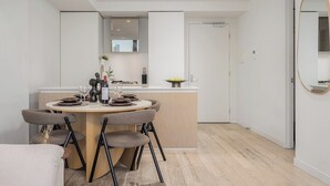 Uma cozinha moderna com uma ilha central, armários brancos e uma área de jantar com cadeiras.