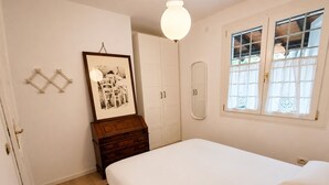 A bedroom with a bed, a dresser, a framed picture, a wardrobe, and a window with curtains.