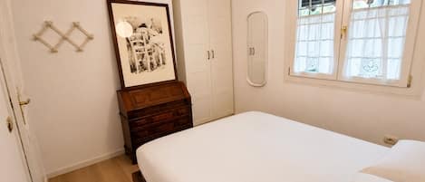 A bedroom with a bed, a dresser, a framed picture, a wardrobe, and a window with curtains.