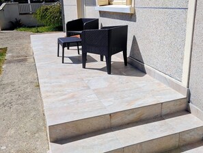 Eine Terrassenfläche mit zwei Korbstühlen und einem kleinen Tisch, einem Fliesenboden aus Stein und einer Betonkante.