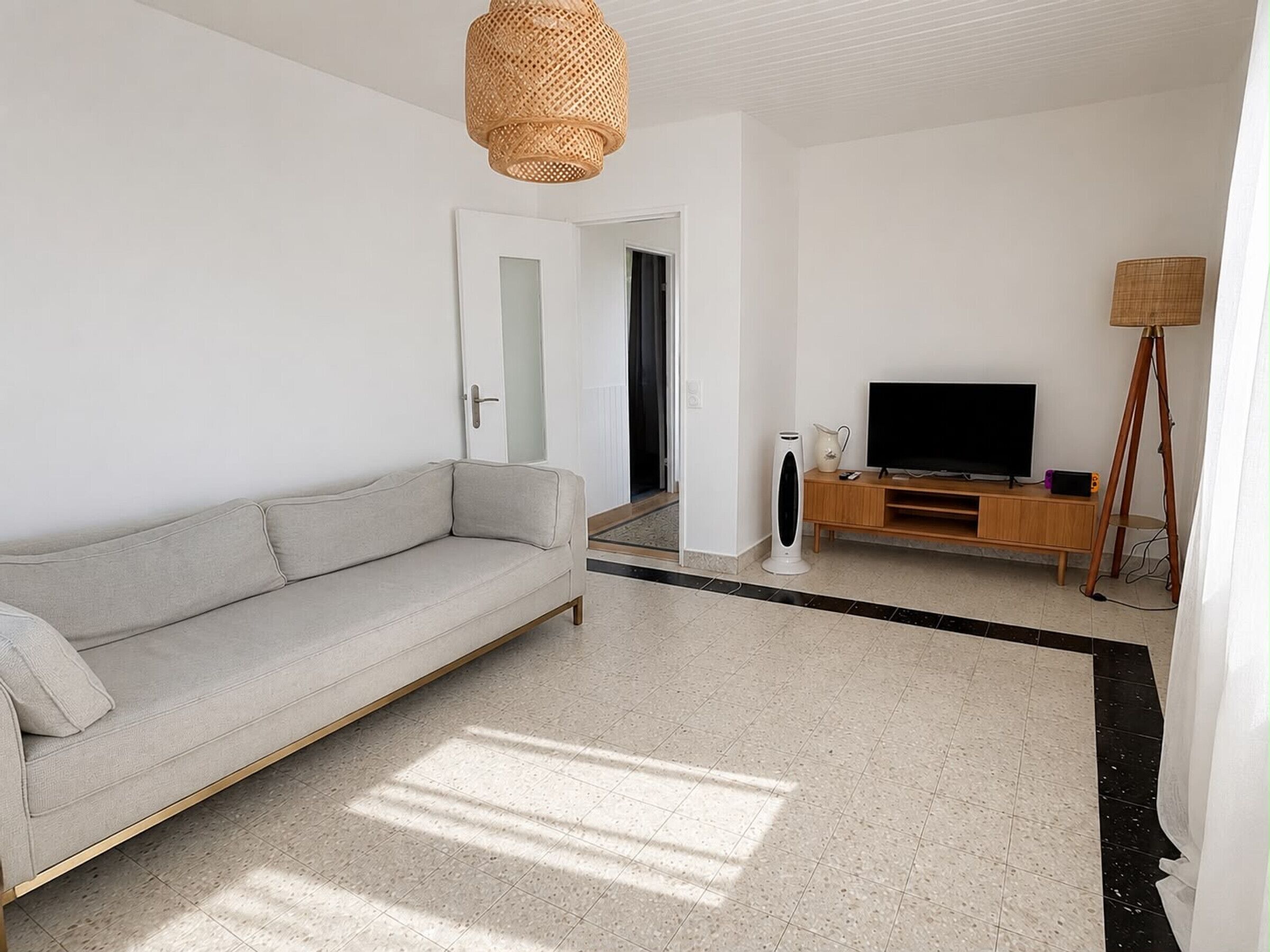 A modern living room with a sofa, a television on a wooden stand, a floor lamp, and a large mirror.