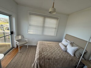 Ein Schlafzimmer mit Bett, Sessel, Fenster mit Jalousien und einer Pendelleuchte.
